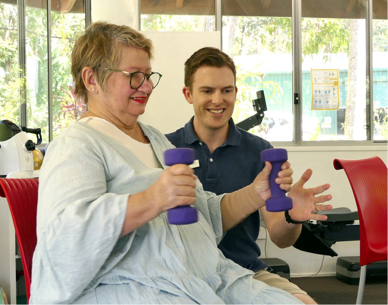 Lady sitting holding arm weights with male assisting exercise